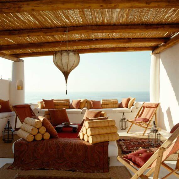 Mediterranean outdoor lounge with white built-in sofas, earth-toned cushions, woven pergola and sea views at the Outside In villa in Salina.