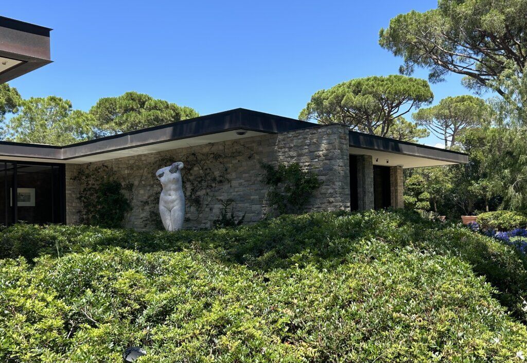 Organic Luxury Villa in Saint-Tropez — Architecture Merging Nature and Living Spaces | Primadesign External view from the a luxury villa in Saint-Tropez designed by Primadesign, featuring organic architecture, stone walls, lush Mediterranean garden, and a Fabio Viale sculpture.