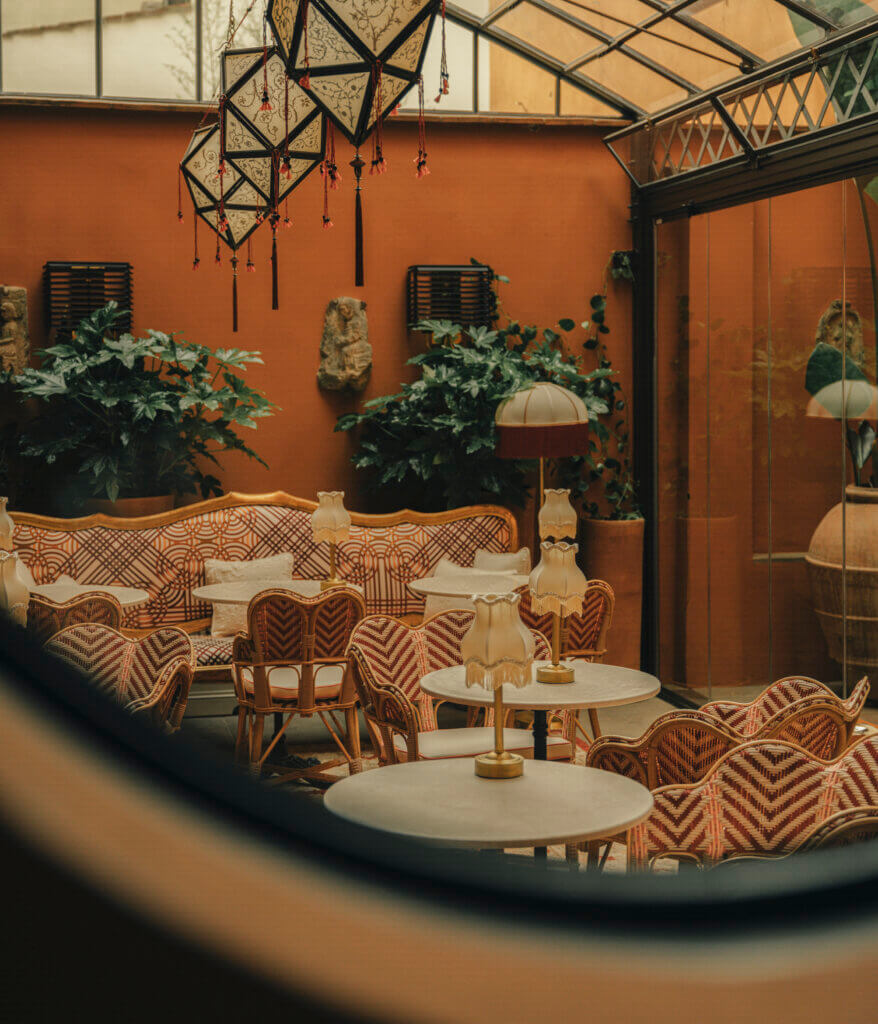 View through an oval window into The James glass veranda in Florence, featuring warm lighting, geometric lanterns, and elegant interior details.