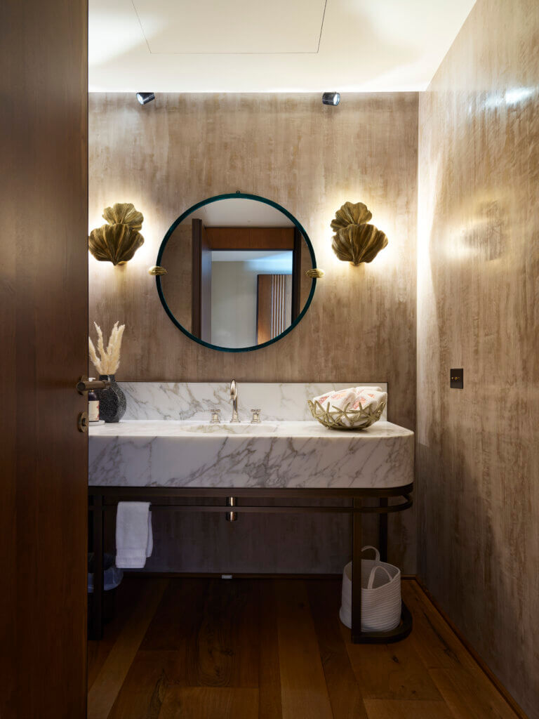 Sculptural Shell-Inspired Bathroom — Saint-Tropez Villa Bathroom with textured shell-like wall lights, round mirror, marble vanity, and warm materials in the Saint-Tropez villa by Primadesign.