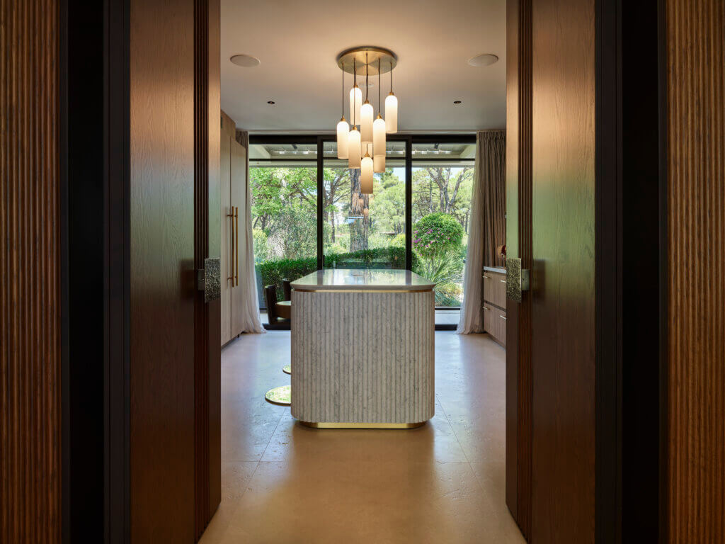 Custom Marble Kitchen Island with Soft Curves — Saint-Tropez Villa Custom marble kitchen island with rounded edges in Primadesign’s Saint-Tropez villa, framed by wooden doors and overlooking the Mediterranean garden through full-height glazing.